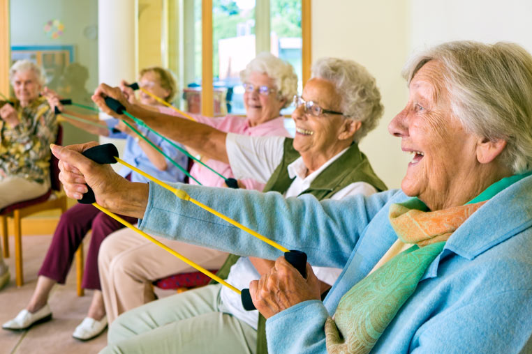 Older ladies smile whilst taking part in a seated exercise class.